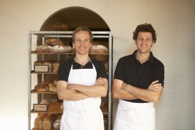 Two male bakers wearing aprons standing with arms crossed, portrait